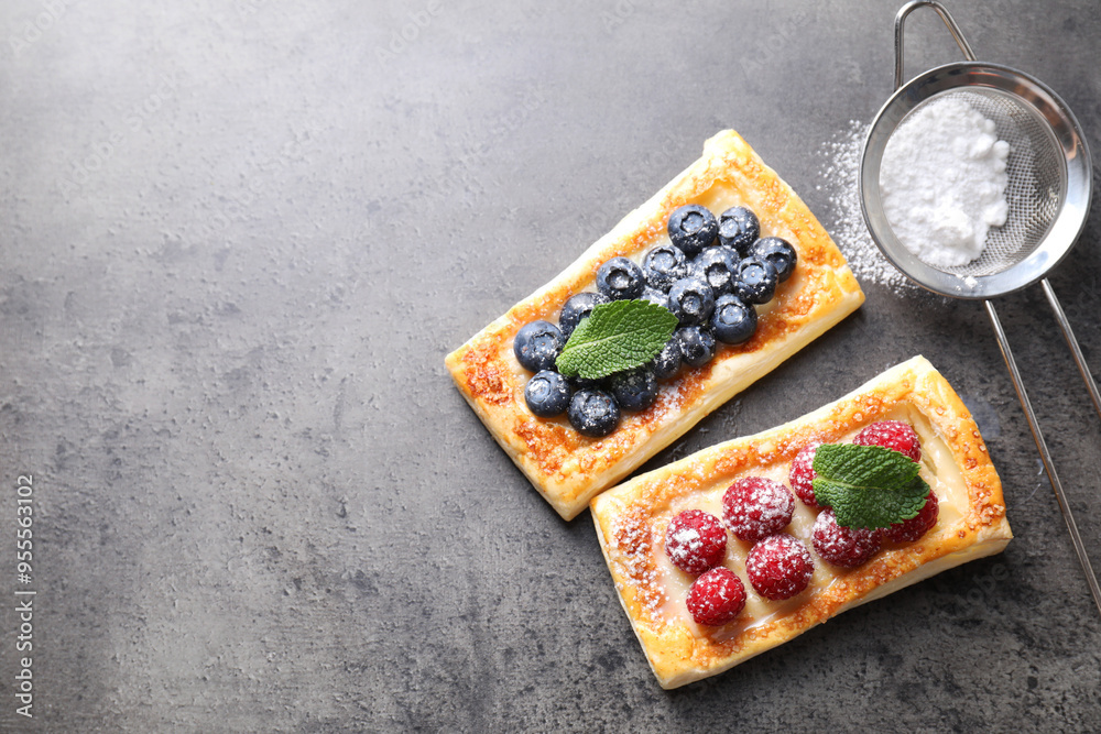 Poster Tasty puff pastries with berries and powdered sugar on grey table, flat lay. Space for text