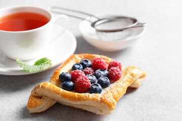 Tasty puff pastry with berries and tea on white table, closeup