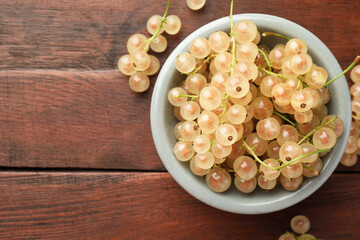 Fresh white currant berries in bowl on wooden table, top view. Space for text