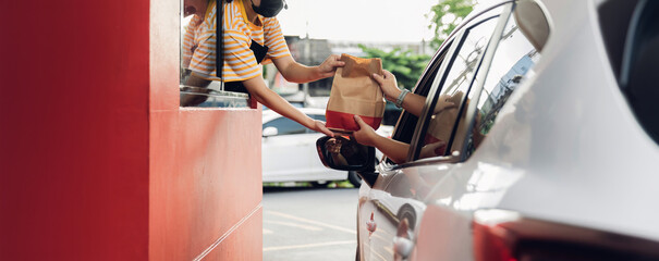 Hand Man in car receiving coffee in drive thru fast food restaurant. Staff serving takeaway order for driver in delivery window. Drive through and takeaway for buy fast food for protect covid19.
