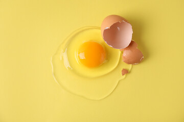 Broken raw egg and shell on yellow background, top view