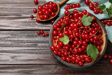 Fresh red currants and green leaves on wooden table, flat lay. Space for text
