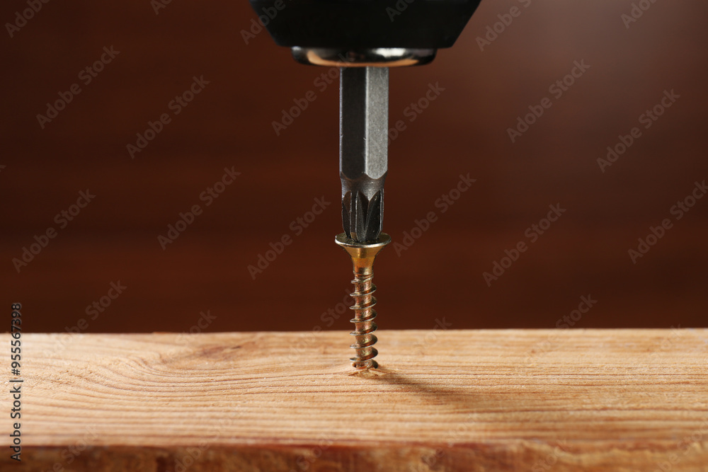 Wall mural screwing screw into wooden plank against brown background, closeup