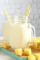 Tasty pineapple smoothie in mason jars and fresh fruit on table