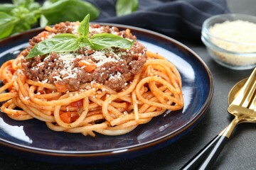 Delicious pasta bolognese with basil served on black table, closeup