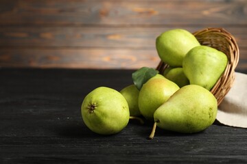 Fresh green pears and wicker basket on black wooden table. Space for text
