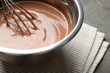 Chocolate dough and whisk in bowl on grey table, closeup