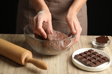 Woman kneading chocolate dough at wooden table, closeup