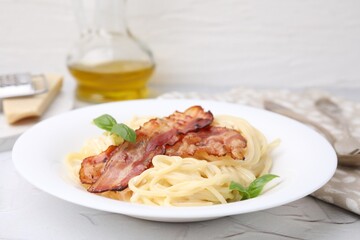 Delicious pasta Carbonara with bacon and basil on light table, closeup