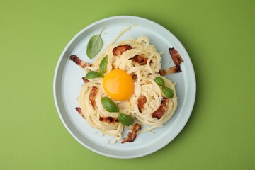 Delicious pasta Carbonara with egg yolk, bacon and basil on green table, top view