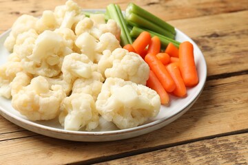Tasty cauliflower with baby carrots and celery on wooden table, closeup
