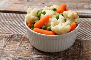 Tasty cauliflower with baby carrots and green peas on wooden table, closeup