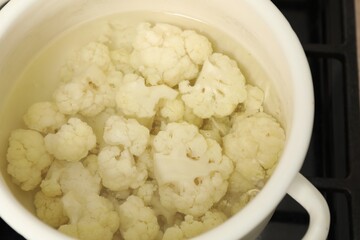 Cooking cauliflower. Florets in white pot with water on cooktop, closeup