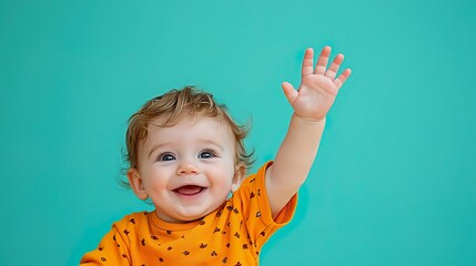 Joyful baby wearing orange shirt, smiling and waving, against a vibrant turquoise background.