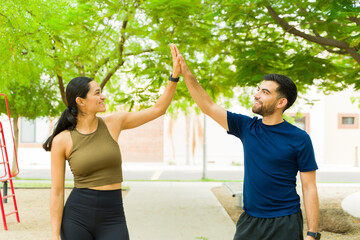 Hispanic young couple in athletic attire celebrating with a high five after working out in the park