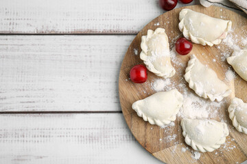 Raw dumplings (varenyky) and fresh cherries on white wooden table, top view. Space for text