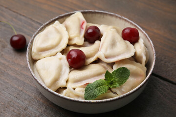 Traditional Ukrainian dumplings (varenyky) with cherries on wooden table, closeup