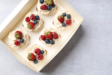 Tasty cupcakes with different berries in box on light grey table, top view. Space for text