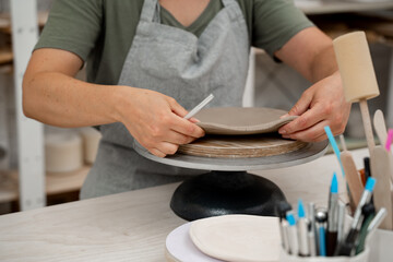 Using a sharp pottery carving knife to cut out a perfect round shape from clay. Ceramics class. Modeling clay into a round form.