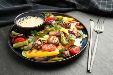 Delicious salad with grilled vegetables and sauce served on dark gray textured table