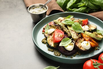 Delicious salad with grilled vegetables, pesto sauce and basil on gray textured table, closeup. Space for text