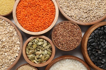Different types of cereals, seeds and legumes in bowls on white table, flat lay