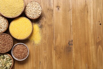 Different types of seeds and cereals in bowls on wooden table, flat lay. Space for text