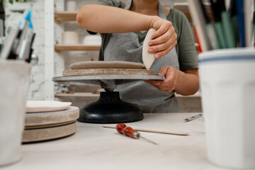 Girl is using a pottery scrapper to smooth the edges of a clay product. Crafting smooth angle conversion and textured ribs with a clay pottery scrapper.