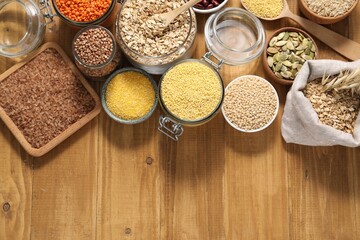 Different types of cereals, legumes and seeds on wooden table, flat lay. Space for text