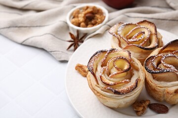 Freshly baked apple roses and walnuts on white tiled table, closeup. Puff pastry