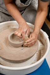 Girl is making smooth edges of pottery with a wooden scraper and a pottery wheel. Cutting the lines on sides of a clay product with a wooden scraper.