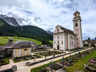 Small Catholic parish church dedicated to St. Peter and St. Paul with a small bell tower and pink walls surrounded by a small cemetery in the cozy village of Sexten (Sesto) in South Tyrol, Dolomites