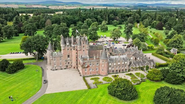 Drone view of Glamis Castle with towers and beautiful garden in Scotland. Aerial view of Scottish landmark with thick walls, and a modern parapet.