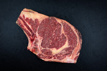 Raw dry aged chianina rib of beef steak offered as top view on a black design board