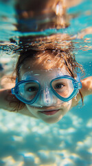 Fototapeta premium Young girl happily swims underwater in a pool with a blue diving mask, surrounded by bubbles and sunlight