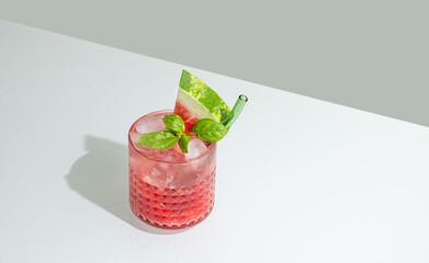 Glass of refreshing watermelon smoothie with basil, ice on white and green background with shadow.
