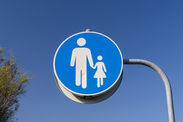 Pedestrian sign with adult and child holding hands on blue sky background