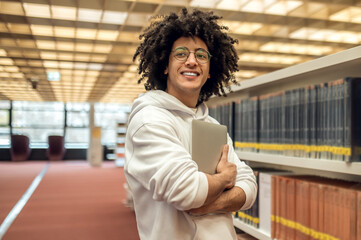 Young man in library taking book from shelf preparing for exams