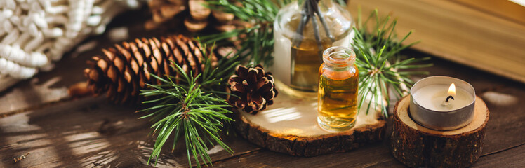 Natural aromatic scented reed diffuser air freshener bottle on wooden table with pine cone, burning candles. Christmas inspiration and mood, cozy home atmosphere, relax. Aromatherapy and decor banner