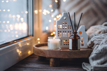 Aroma diffuser, burning candle, Christmas perfume on wooden bamboo tray, knitted sweater. Cozy home decor, hygge and aromatherapy concept. Comfortable atmosphere, Scandinavian decor.