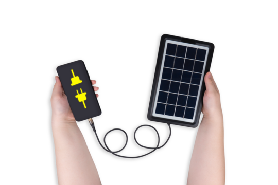 A portable solar panel in one hand is connected to a smartphone in the other hand on a transparent background (close-up). The smartphone screen shows an icon in the form of an electrical connection