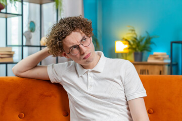 Thoughtful Caucasian man guy male sitting at home looks pensive thinks over life concerns or...