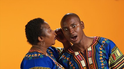 Obraz premium Smiling woman sharing important secret with her husband, whispering in his ear and telling gossip. Shocked man leaning in and listening to confidential information, secrecy concept.