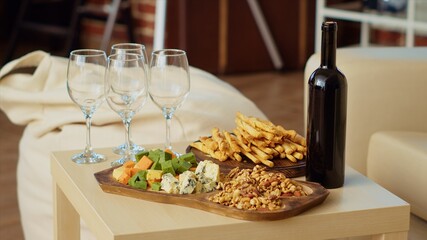 Close up shot of charcuterie board and gourmet cheese platter set up by hosts to properly welcome guests arriving soon at apartment party. Wine bottle and glasses next to appetizers in living room