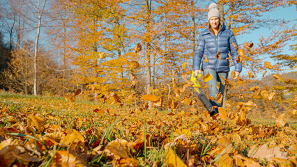 Hardworking woman operates a leaf blower amidst a colourful autumnal setting. Young lady clearing...