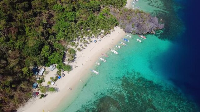 Aerial view of beautiful white sand beach, with palm trees and filipino boats in Siete Pecados Beach, Palawan, Philippines. 
