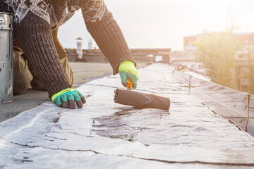 a young worker treats a roof with bitumen primer before applying rolled asphalt roofing using a torch © Torkhov
