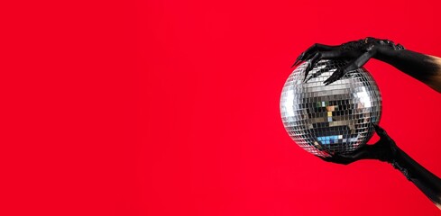 Black hands of witch with disco ball on red background with space for text. Halloween celebration