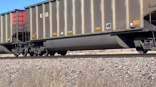 A freight train travels across the desert seen from a low angle, pan focused on wheels while turning left to right.
