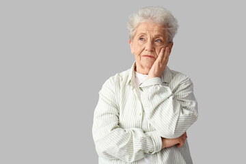 Thoughtful senior woman on grey background